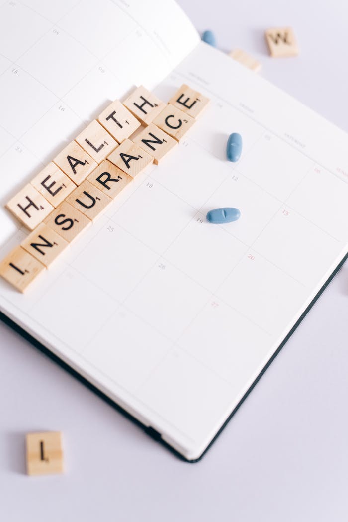 Crafting Captivating Headlines: Your awesome post title goes here Scrabble tiles spelling health insurance on a calendar beside blue pills, symbolizing medication schedule.